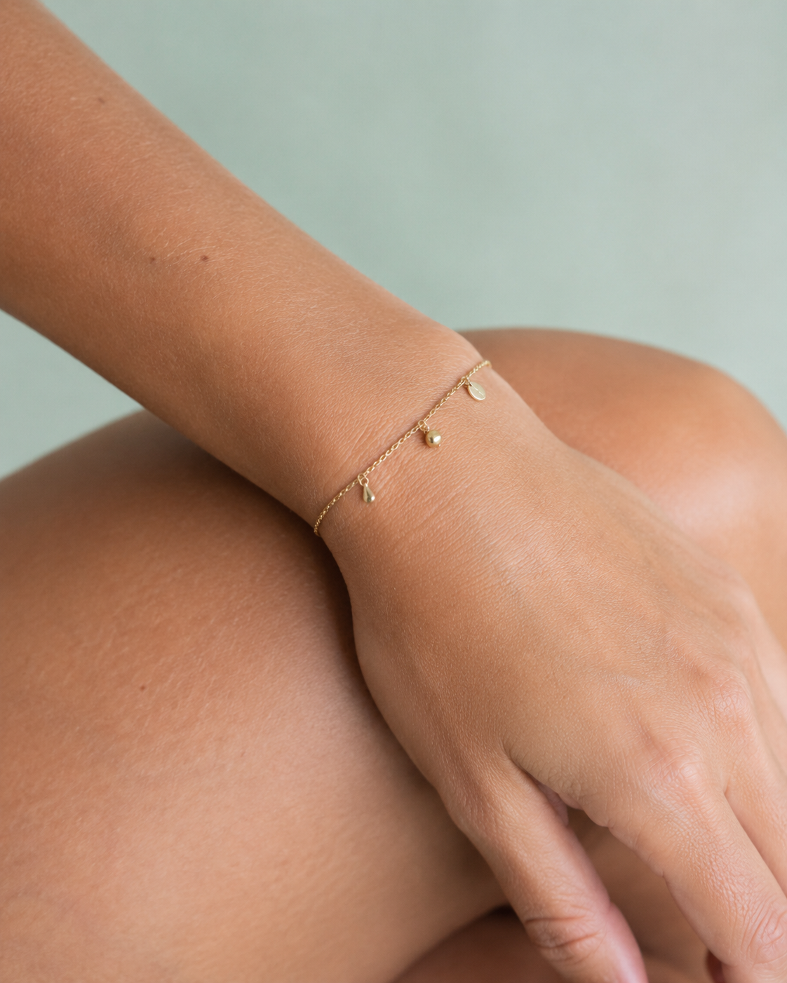 Poignet portant un bracelet en chaîne dorée fine à breloques